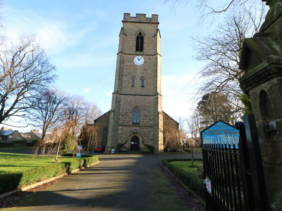 The exterior of a stone church with a clock tower and surrounding trees and driveway at Sparrow House in Alnwick