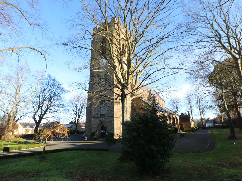 A stone church building with a tower surrounded by leafless trees on a grassy area