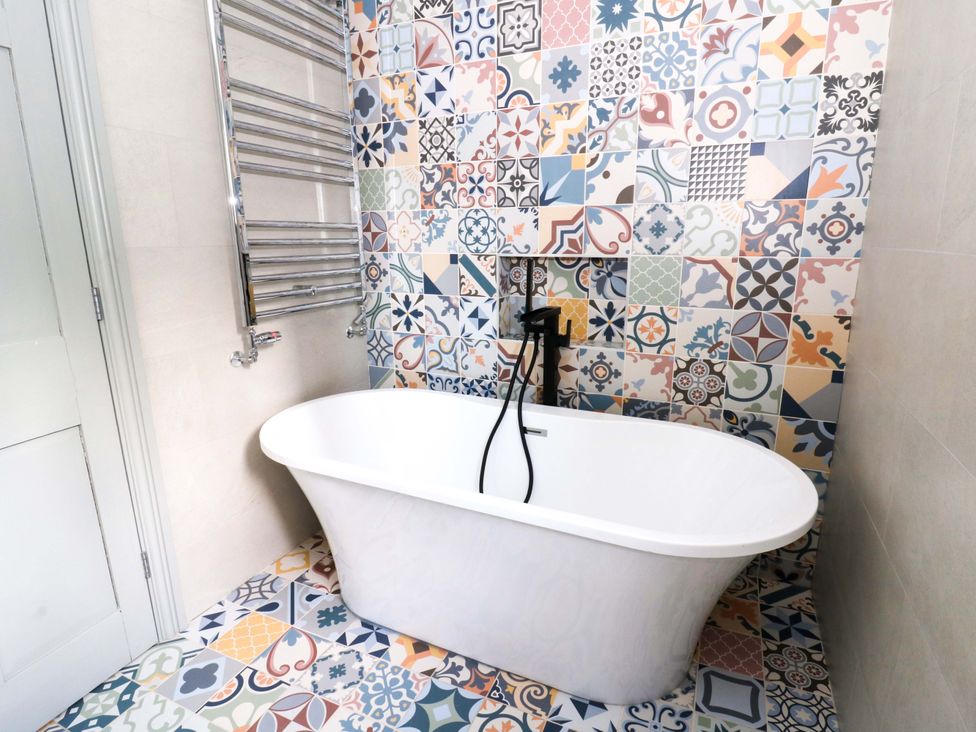 A bathroom featuring a bathtub and decorative wall tiles at Island House Aberaeron