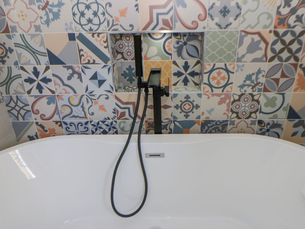 A bathtub with a faucet and patterned wall tiles at Island House Aberaeron