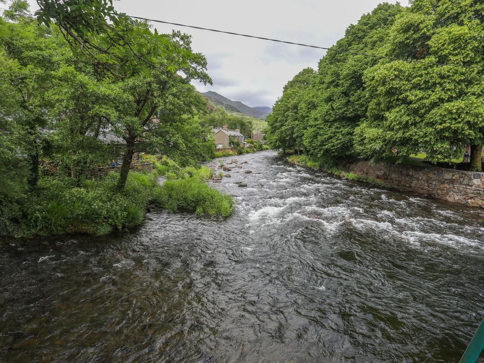 A river with trees and houses along the bank at Ty Capel Bethania in Nant Gwynant