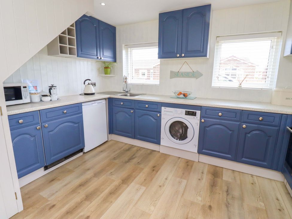 A kitchen with blue cabinets and a washing machine at Lavender Cottage Beadnell
