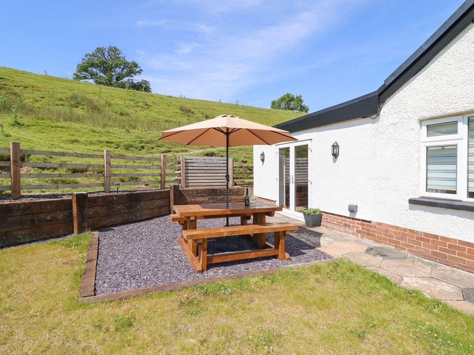 A garden with a wooden table and umbrella at Bryn Bras in Corwen