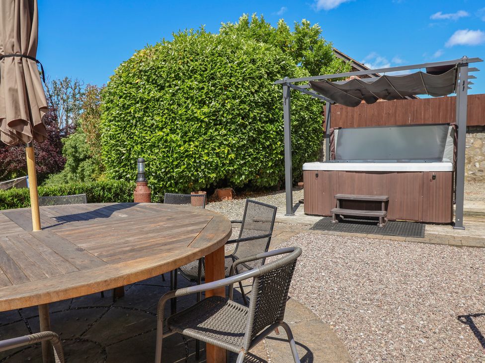 A garden with an outdoor table and chairs and a hot tub at Home Farm St Asaph