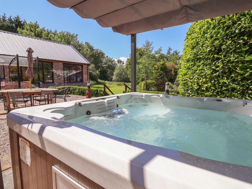 A hot tub on a patio area with dining table at Home Farm, St Asaph