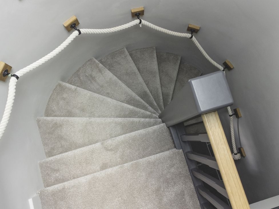 A spiral staircase with a carpet and handrail at Lower Well Farm House in Totnes