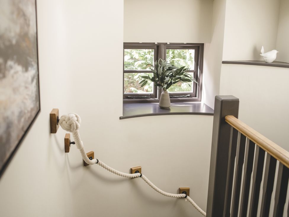 A staircase with a knotted rope railing and a plant on a windowsill at Lower Well Farm House in Totnes