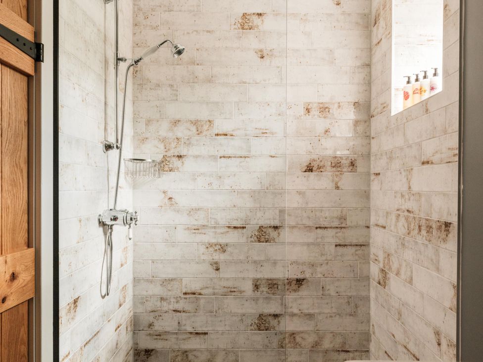 A shower with a wall-mounted shower head and soap dispenser at Lower Well Farm House in Totnes