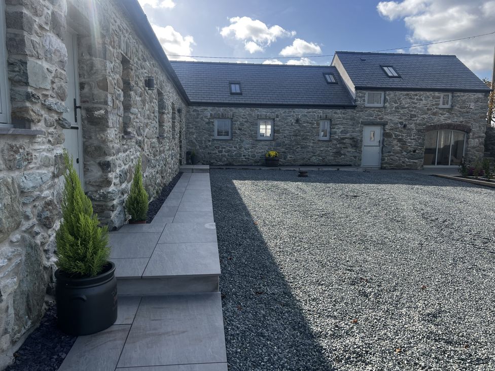 An outdoor area with stone buildings and a gravel path at Beudy Tanrallt in Llanfachraeth