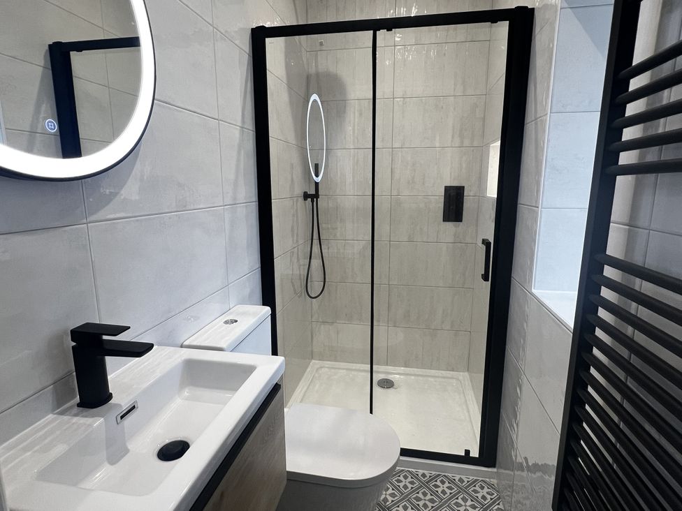 A bathroom with a shower, sink, toilet, and mirror at Beudy Tanrallt in Llanfachraeth