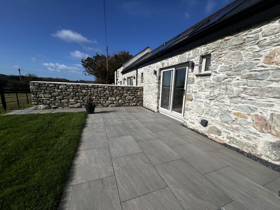 An outdoor area with a stone wall and sliding doors at Beudy Tanrallt in Llanfachraeth