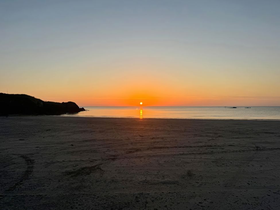 A beach with a sunset over the ocean at Beudy Tanrallt in Llanfachraeth