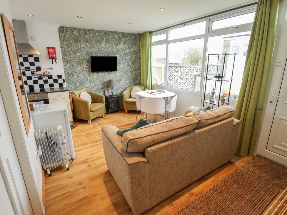 A living room with a sofa, armchairs, and a kitchenette at Seaside Retreat in Chapel Point near Chapel St Leonards
