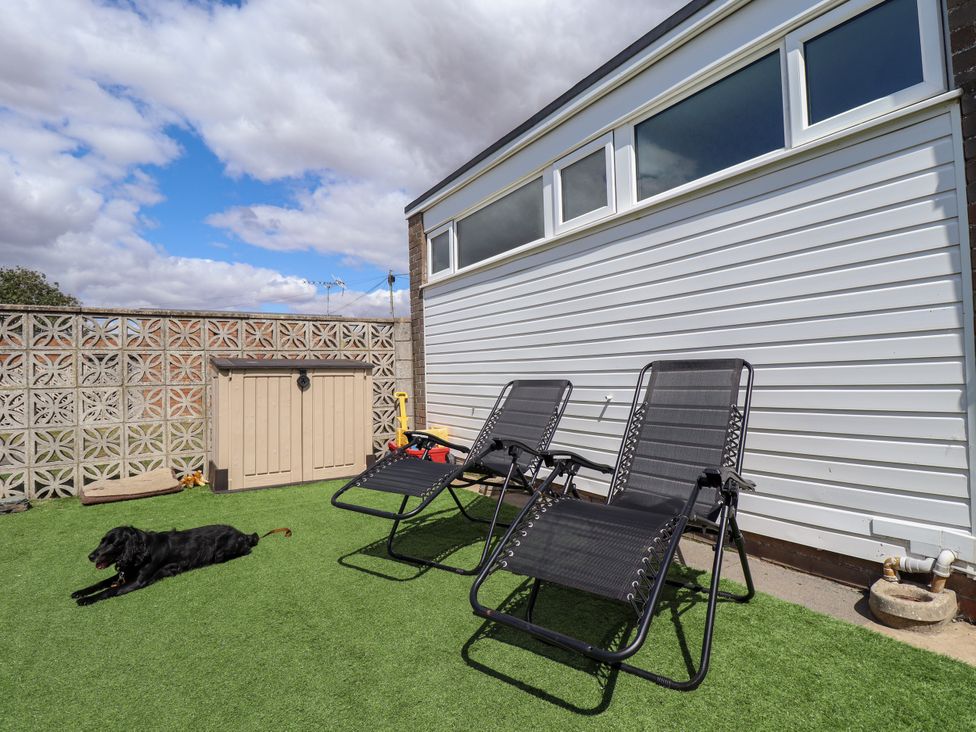A garden with lawn chairs and a dog at Seaside Retreat Chapel Point near Chapel St Leonards