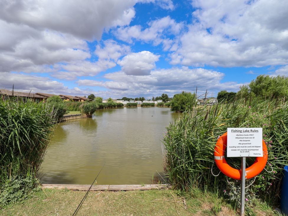A lake with fishing rules sign and wooden pathway at Seaside Retreat Chapel Point near Chapel St Leonards
