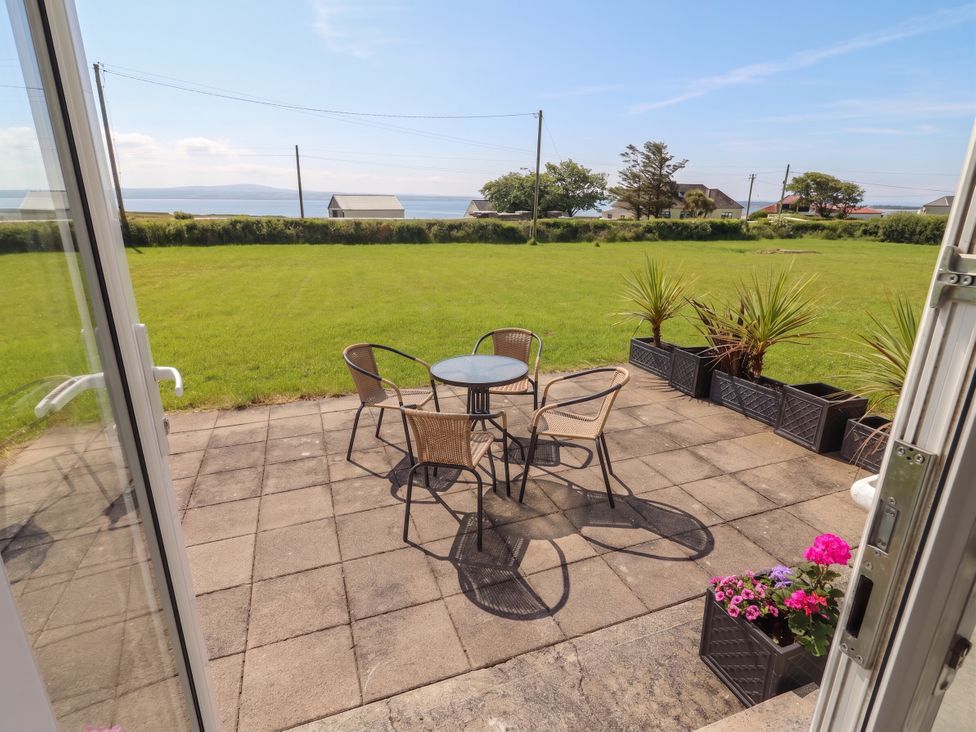 A patio with chairs and a table overlooking a grassy area at The Boathouse in Carrigaholt, County Clare