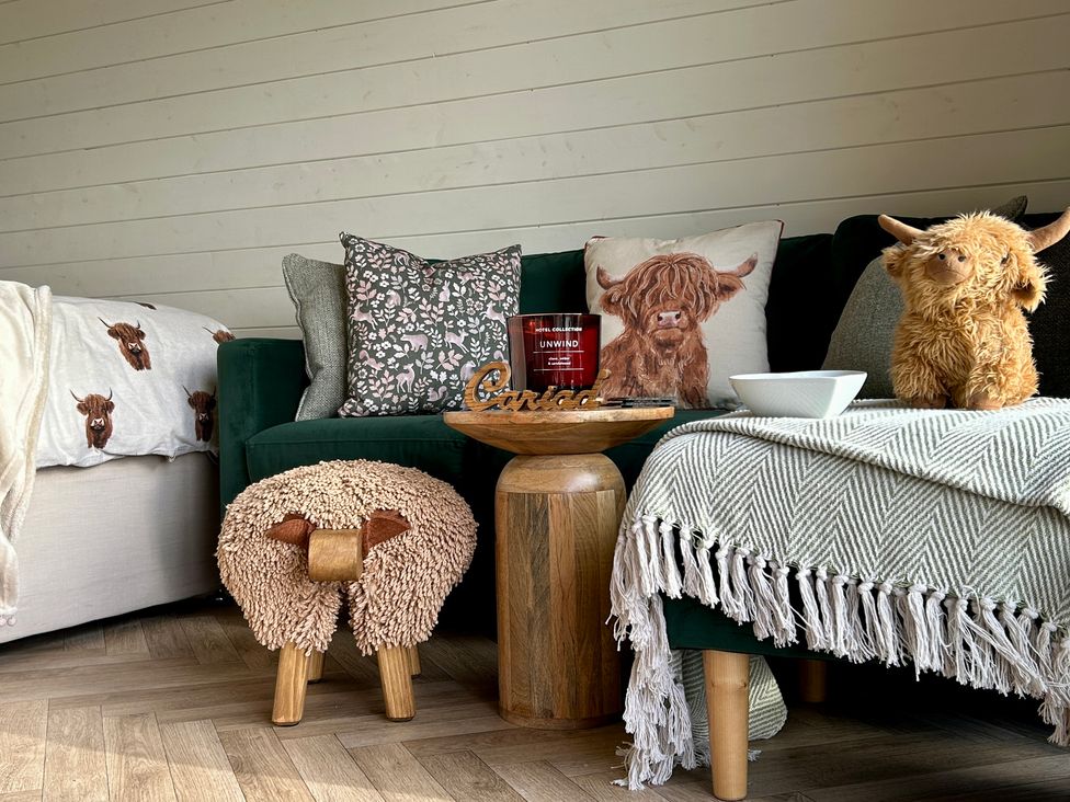 A living room with a couch, pillows, candle, and a wooden table at Willow in Llangurig near Llanidloes