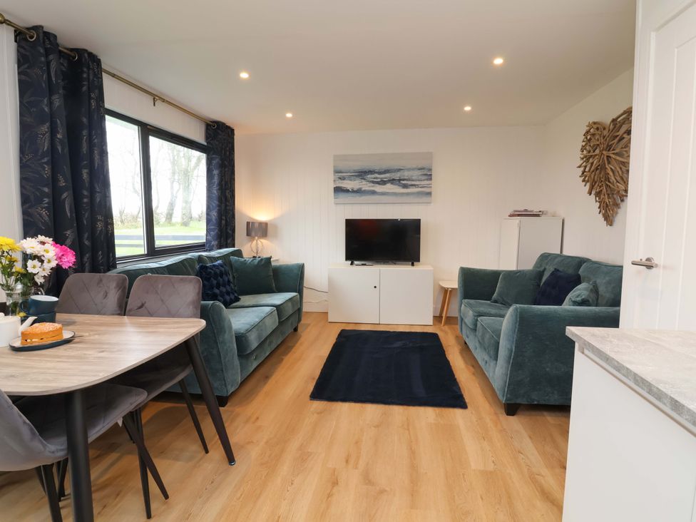 A living room with a sofa, television, and dining table at Cassia in Kilkhampton