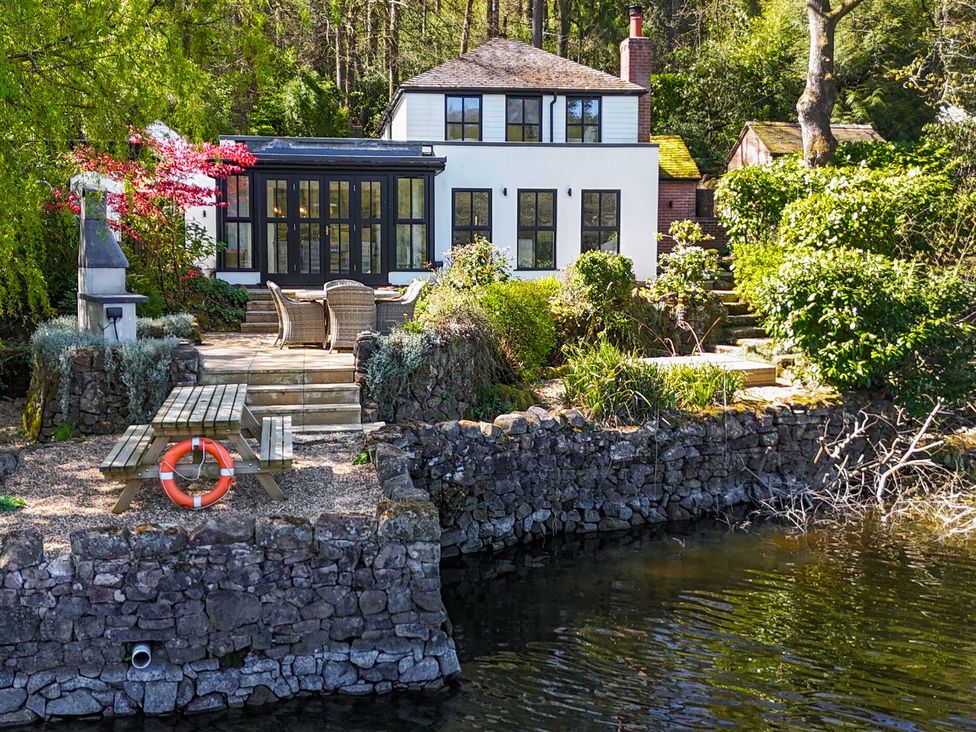 An outdoor area with a house, table, and chairs by the water at The Sheiling Rudyard Lake