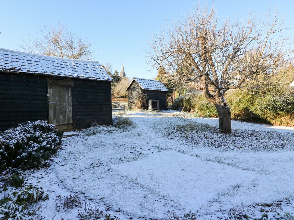 A garden with snow, sheds, trees, and a bench at 66 High Street, Cambridge