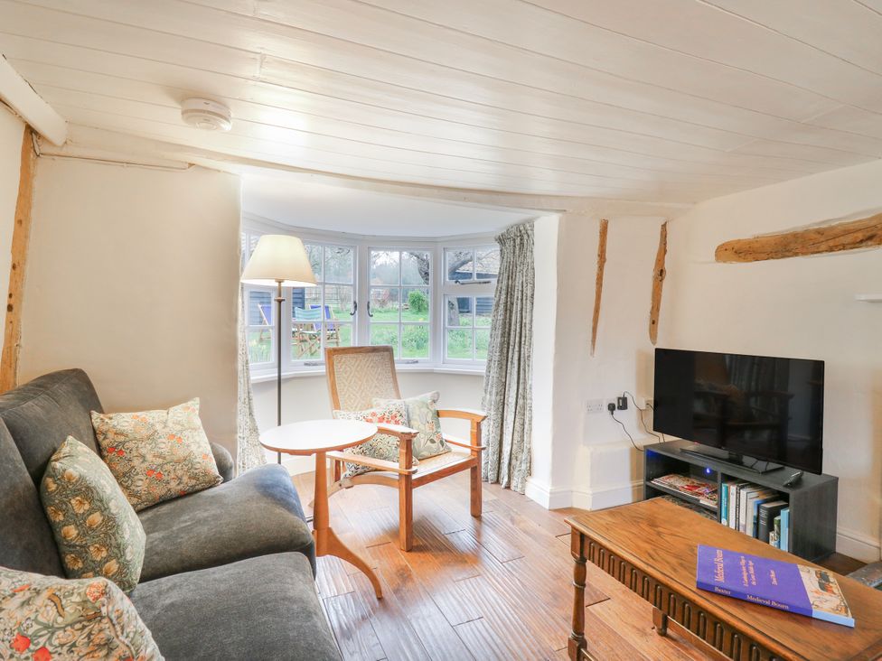 A living room with a sofa, table, lamp, and TV at The Old Smithy in Bourn