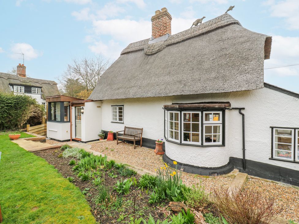 A cottage with a thatched roof and garden at The Old Smithy in Bourn