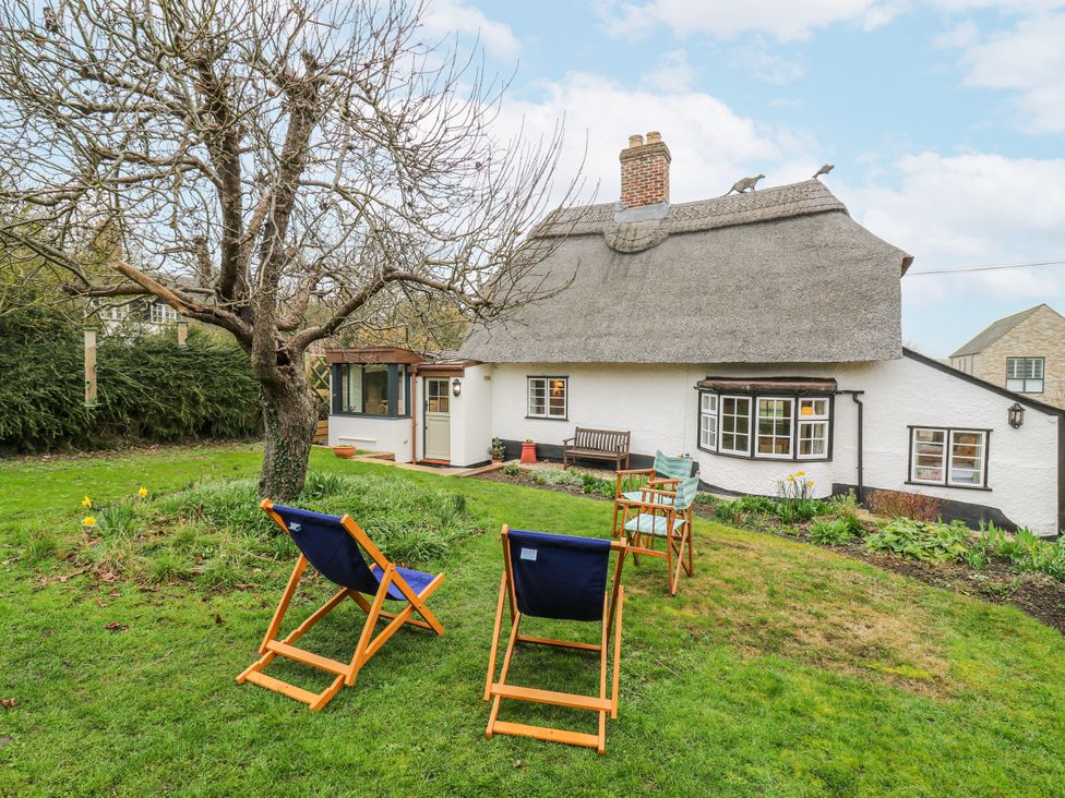 An outdoor view of a house with a garden and chairs at The Old Smithy in Bourn