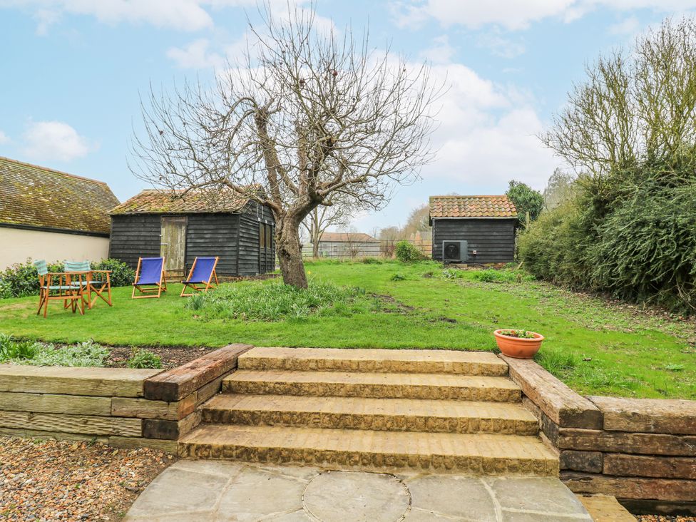A garden with a tree, wooden sheds, and chairs at The Old Smithy in Bourn