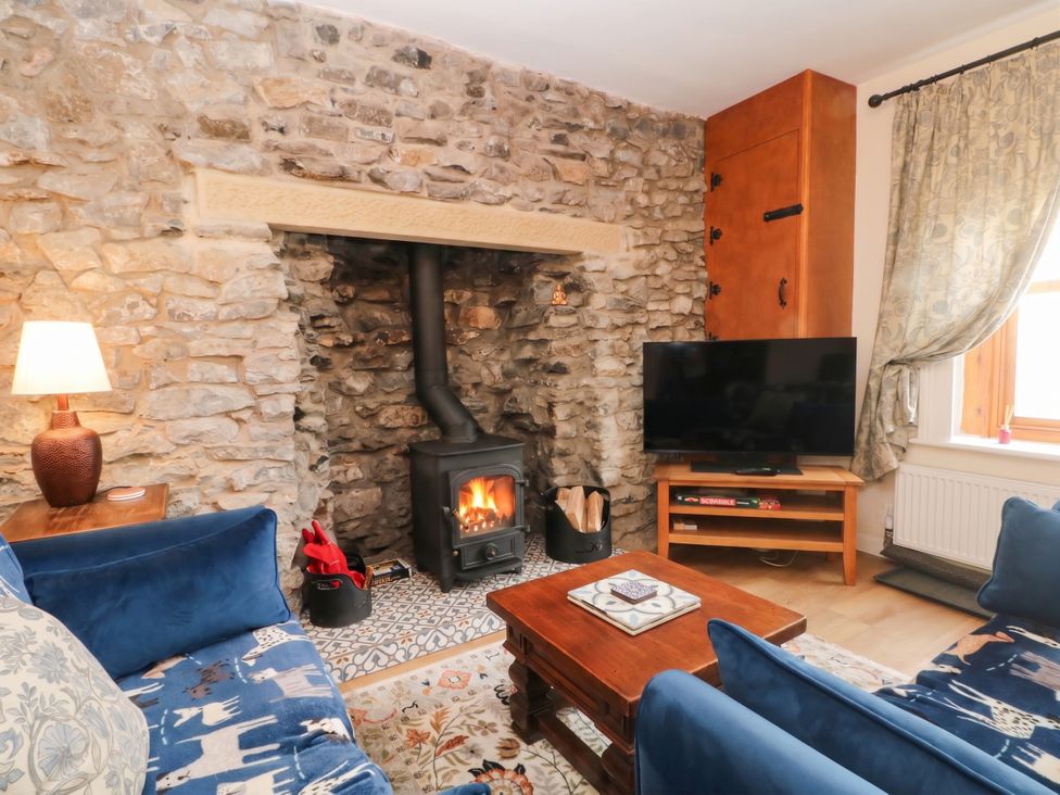 A living room with a stone wall and wood stove at The Cottage O'ergate in Bradwell