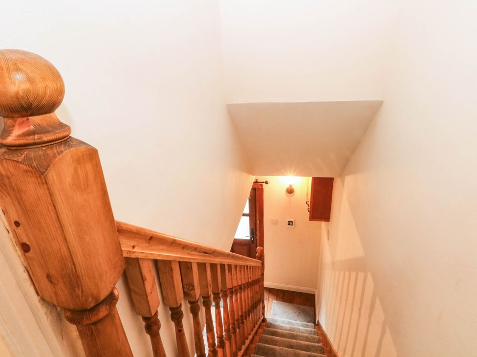 A staircase with wooden handrail and light fixture at The Cottage O'ergate in Bradwell