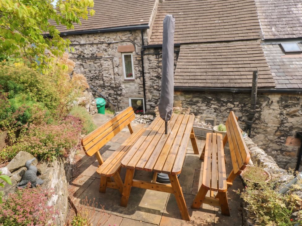 A patio area with a wooden table and benches under a parasol at The Cottage O'ergate in Bradwell
