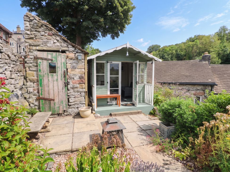 A garden with a stone wall and a green shed at The Cottage O'ergate in Bradwell