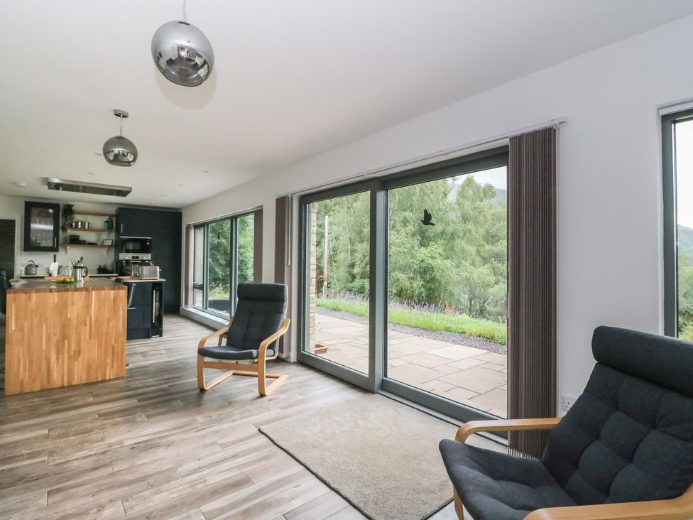 A living room with a kitchen area and large windows at Taigh Creag Thulach in Taynuilt