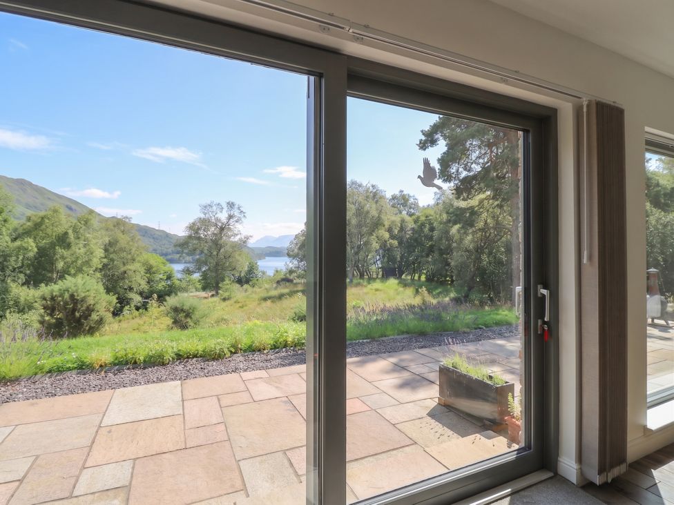 A living room with a sliding glass door opening to a view of the lake and mountains at Taigh Creag Thulach in Taynuilt