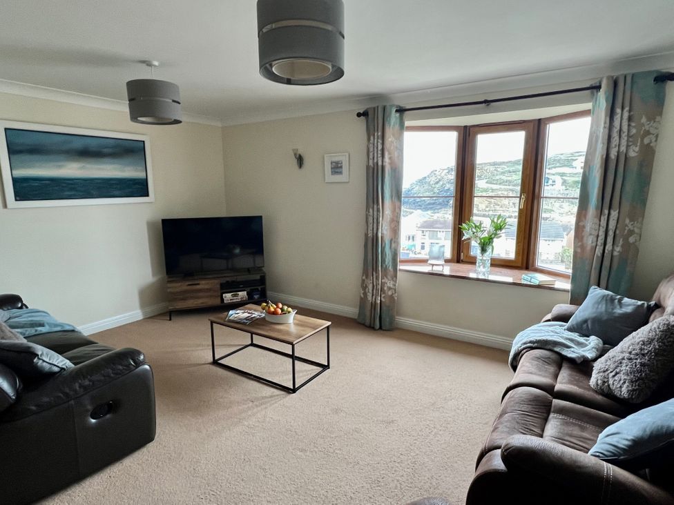 A living room with two sofas a coffee table a television and a window with curtains at Curnows in Portreath