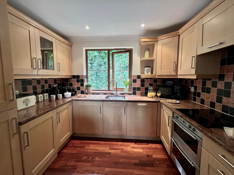 A kitchen with wooden cabinets a countertop with various kitchen items a window above the sink and a tiled backsplash at Curnows in Portreath