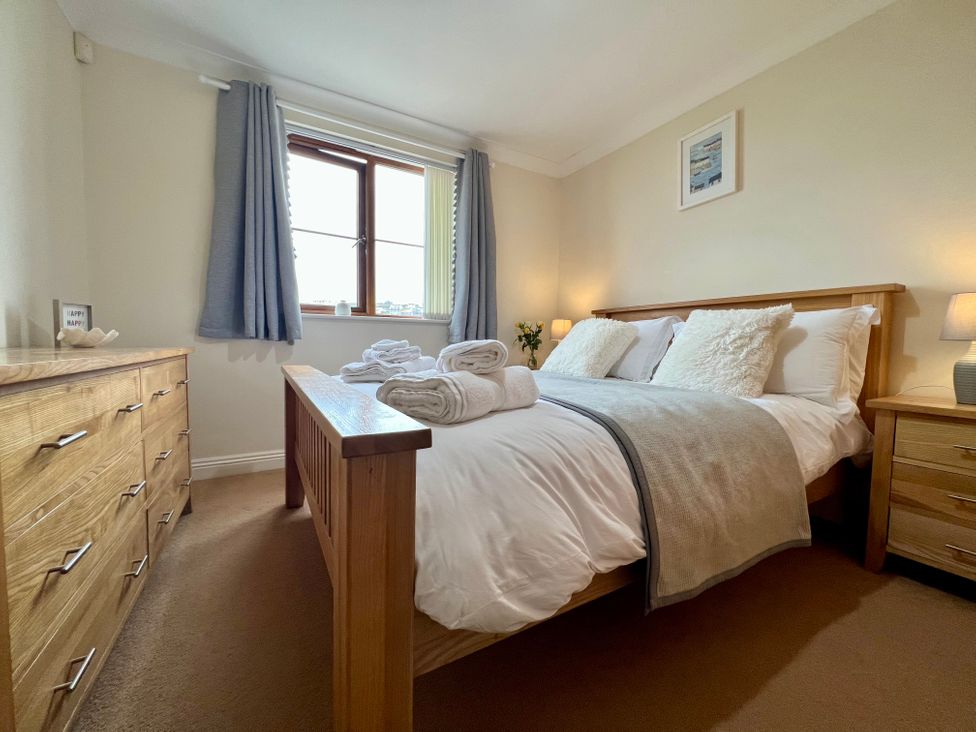 A bedroom with a wooden bed and dresser next to a window with curtains at Curnows in Portreath