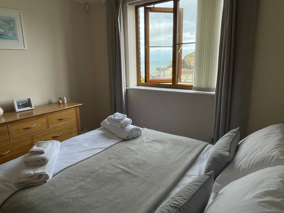 A bedroom with a bed, folded towels on the bed, a wooden dresser, and a window with a view of the sea and cliffs at Curnows in Portreath