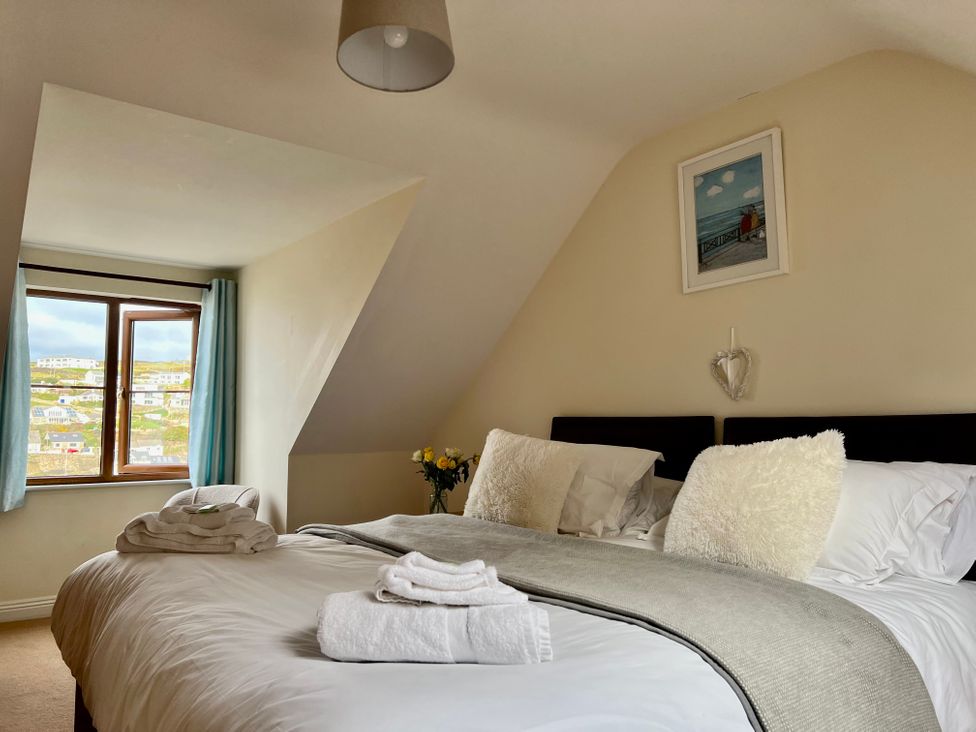 A bedroom with a double bed pillows folded towels window and flowers at Curnows in Portreath