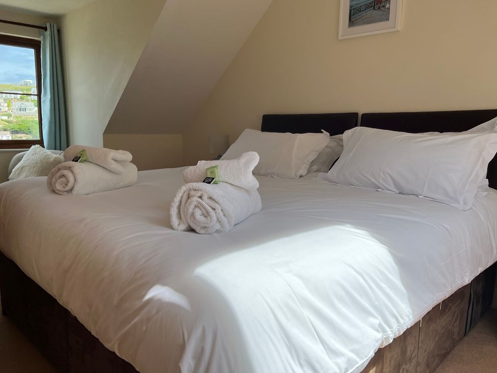 A bedroom with a double bed white pillows and rolled towels near a window with curtains at Curnows Portreath