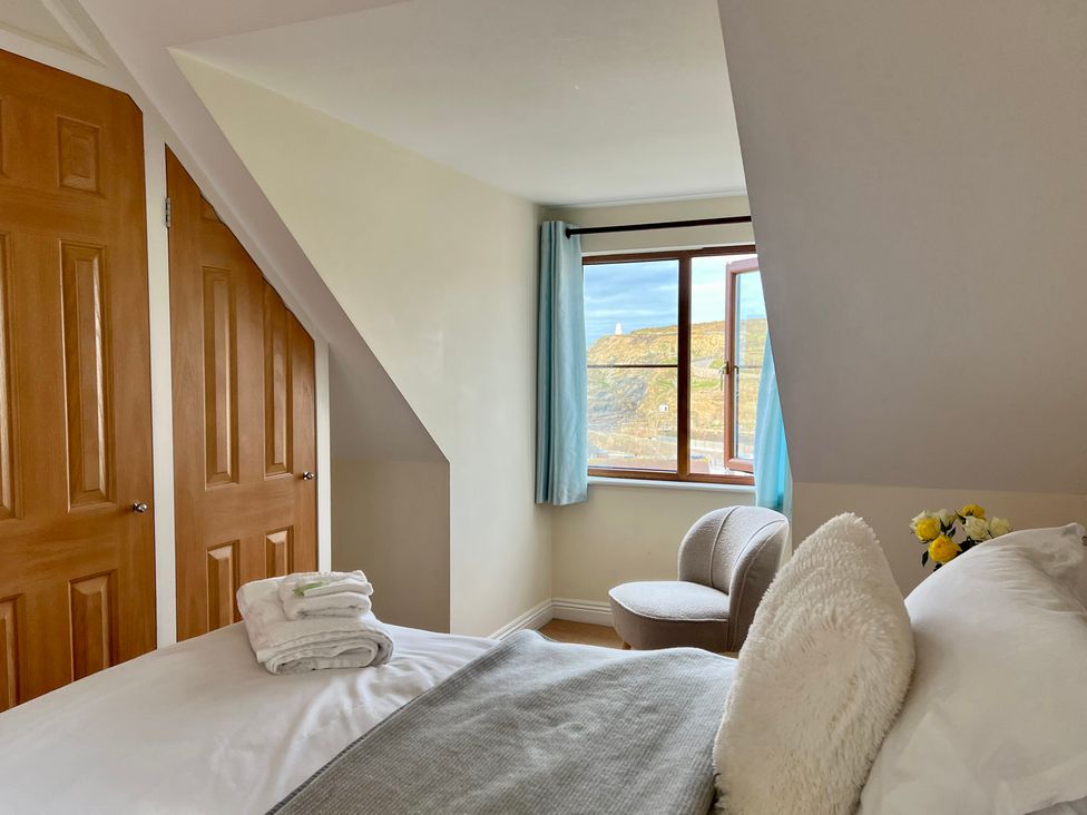 A bedroom with a bed a chair a window with blue curtains and two wooden closet doors at Curnows Portreath
