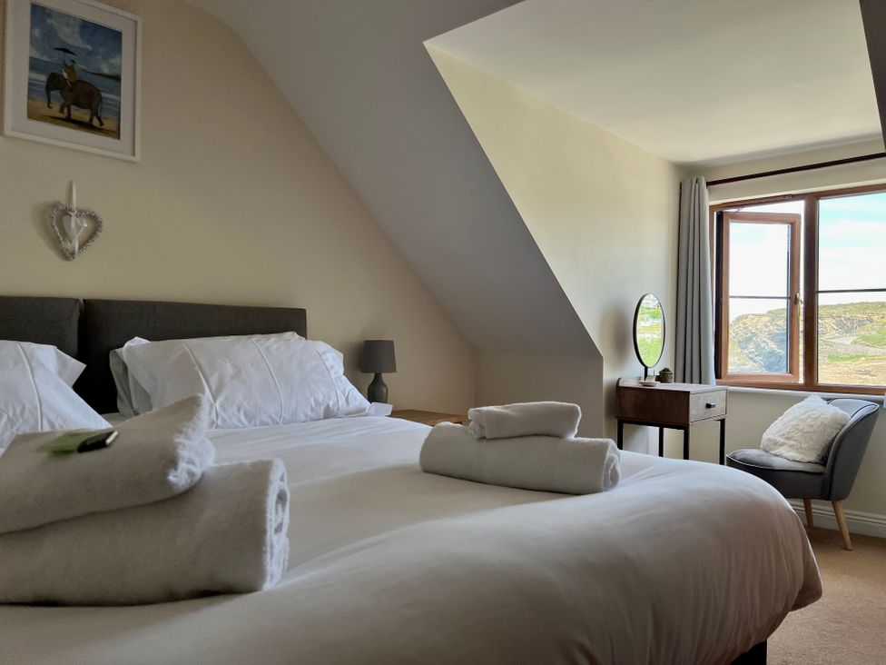 A bedroom with a double bed towels on bed bedside table lamp dressing table chair and window with a view at Curnows in Portreath