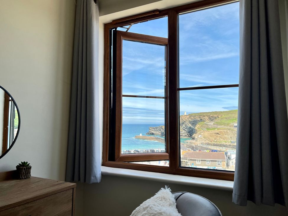 A room with a wooden dresser a round mirror curtains an open window showing a coastal view with cliffs and the ocean at Curnows in Portreath