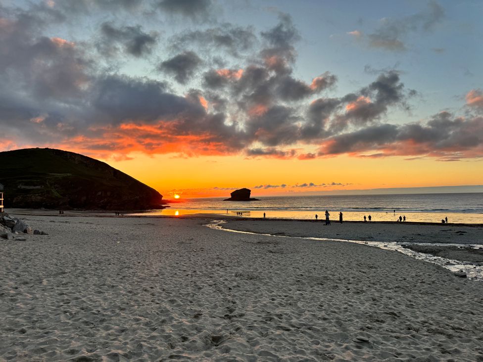 A beach at sunset with people walking near the shoreline and a large rock formation in the water at Curnows in Portreath