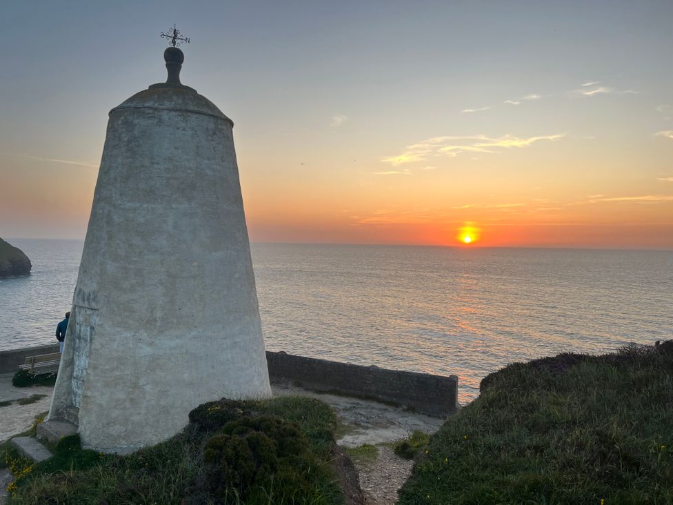 A coastal scene with a large white tower and a sunset over the ocean at Curnows in Portreath