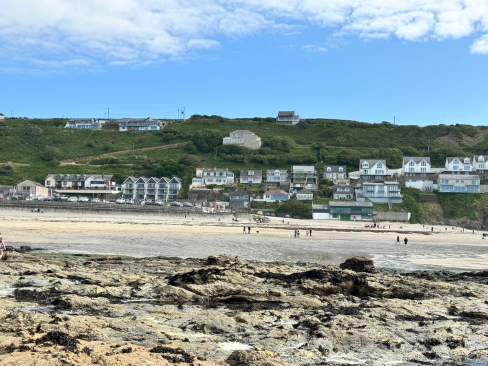 A rocky beach with people walking and houses on a green hillside at Curnows in Portreath