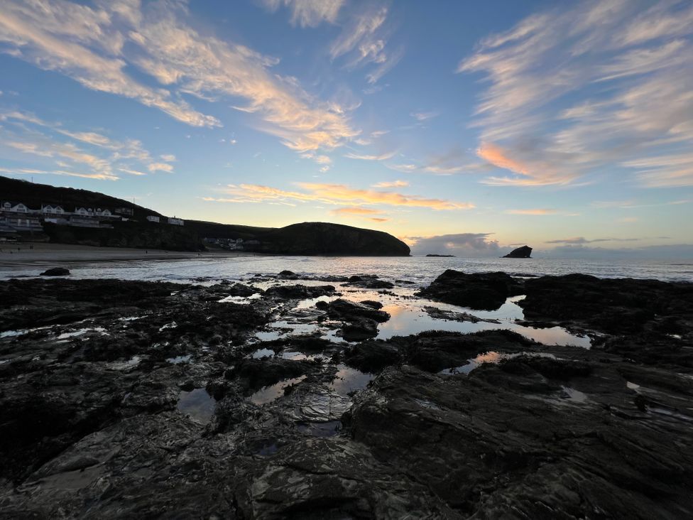 A rocky shoreline with tide pools at sunset and houses on a hill in the background at Curnows in Portreath