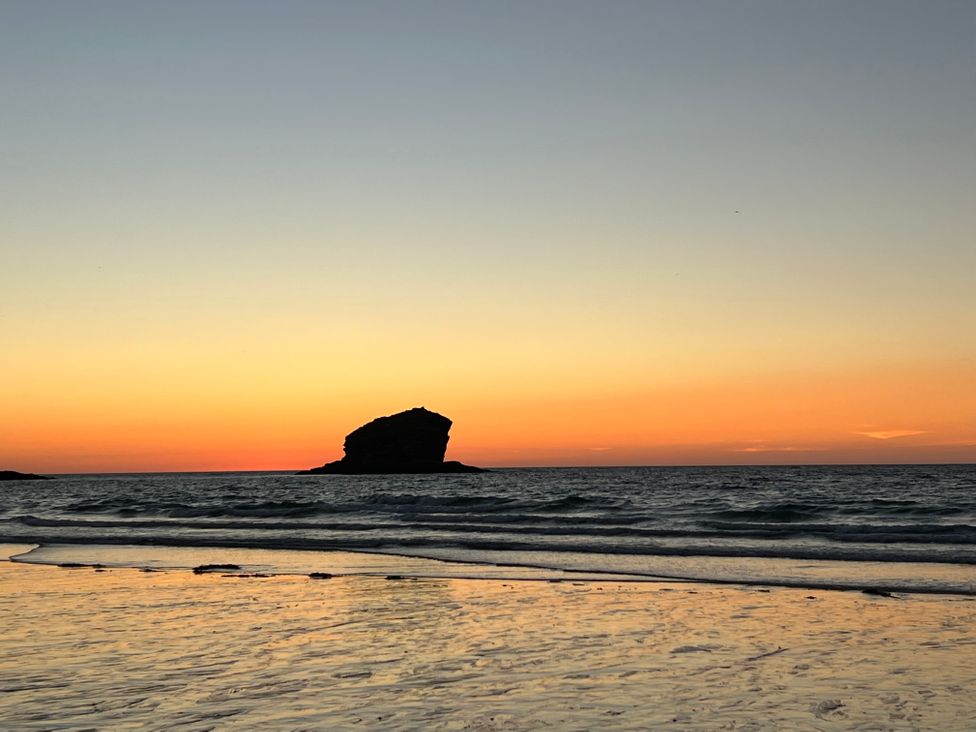 A beach with waves and a rock formation in the sea at sunset at Curnows in Portreath