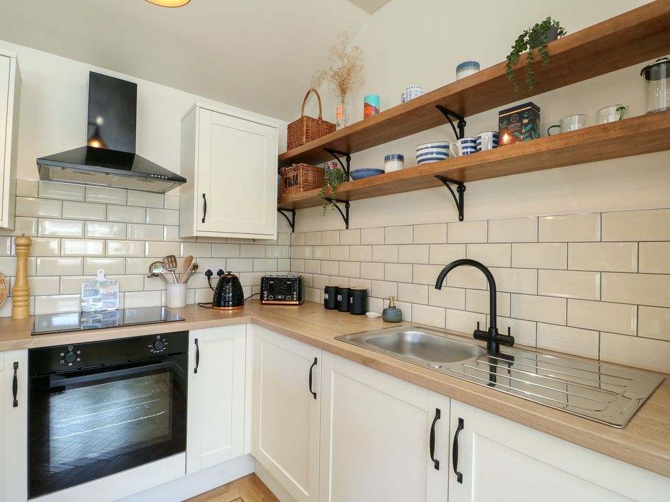 A kitchen featuring a sink, oven, and shelves with kitchenware at Trillo Lodge in Colwyn Bay