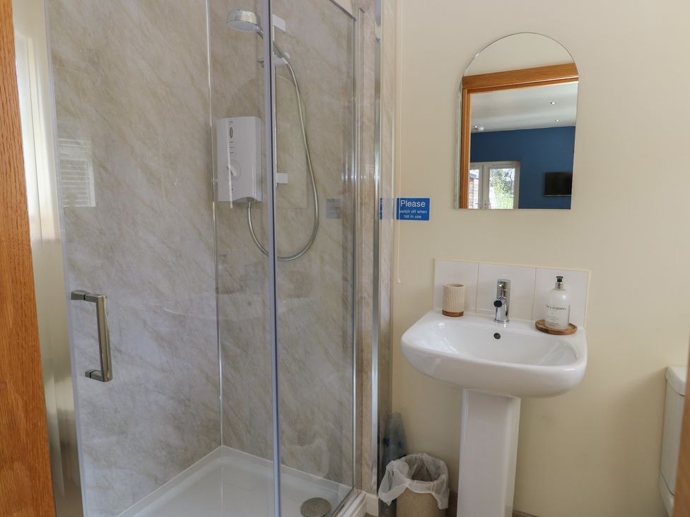 A bathroom with a shower, sink, and mirror at Trillo Lodge in Colwyn Bay